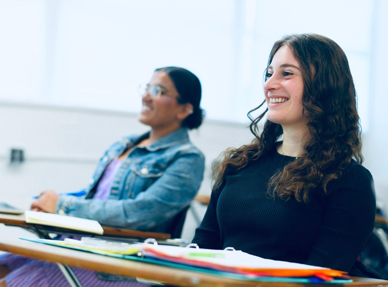 Two female students smiling at desk in classroom