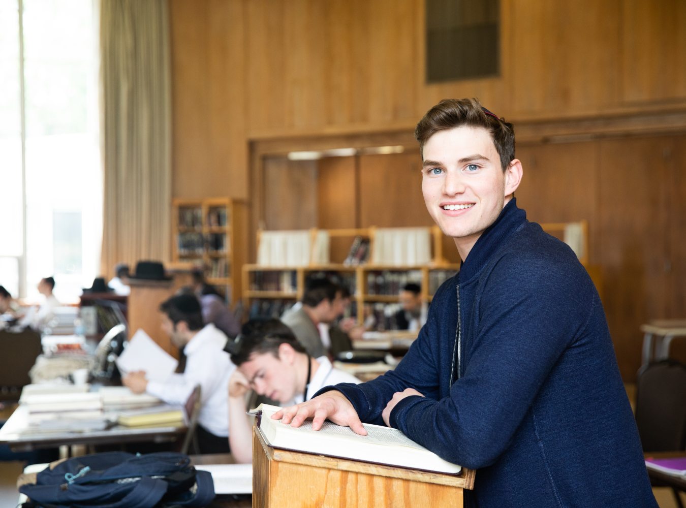 Student smiling with peers reading behind him