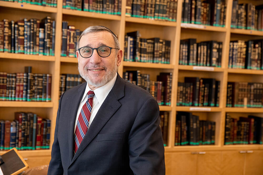 Dean Moshe Sokol wearing a suit and tie and smiling in front of bookcase