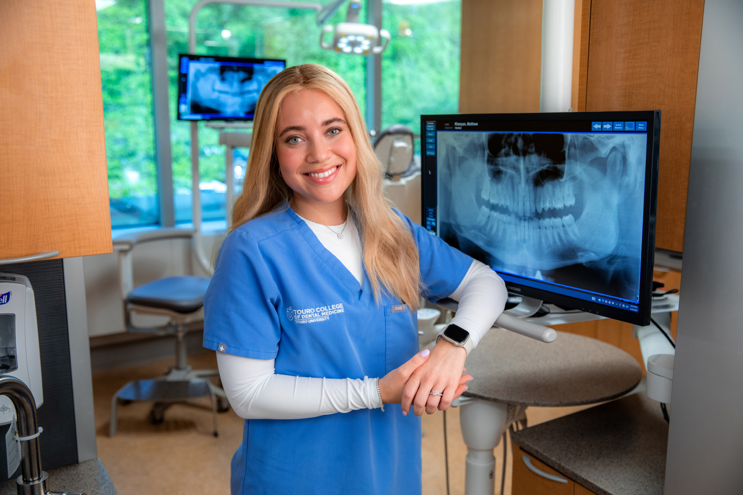 Aliza Silverberg smiling and wearing scrubs next to dental xray on screen.