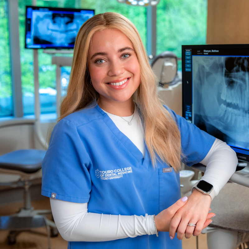 Aliza Silverberg smiling and wearing scrubs next to dental xray on screen.