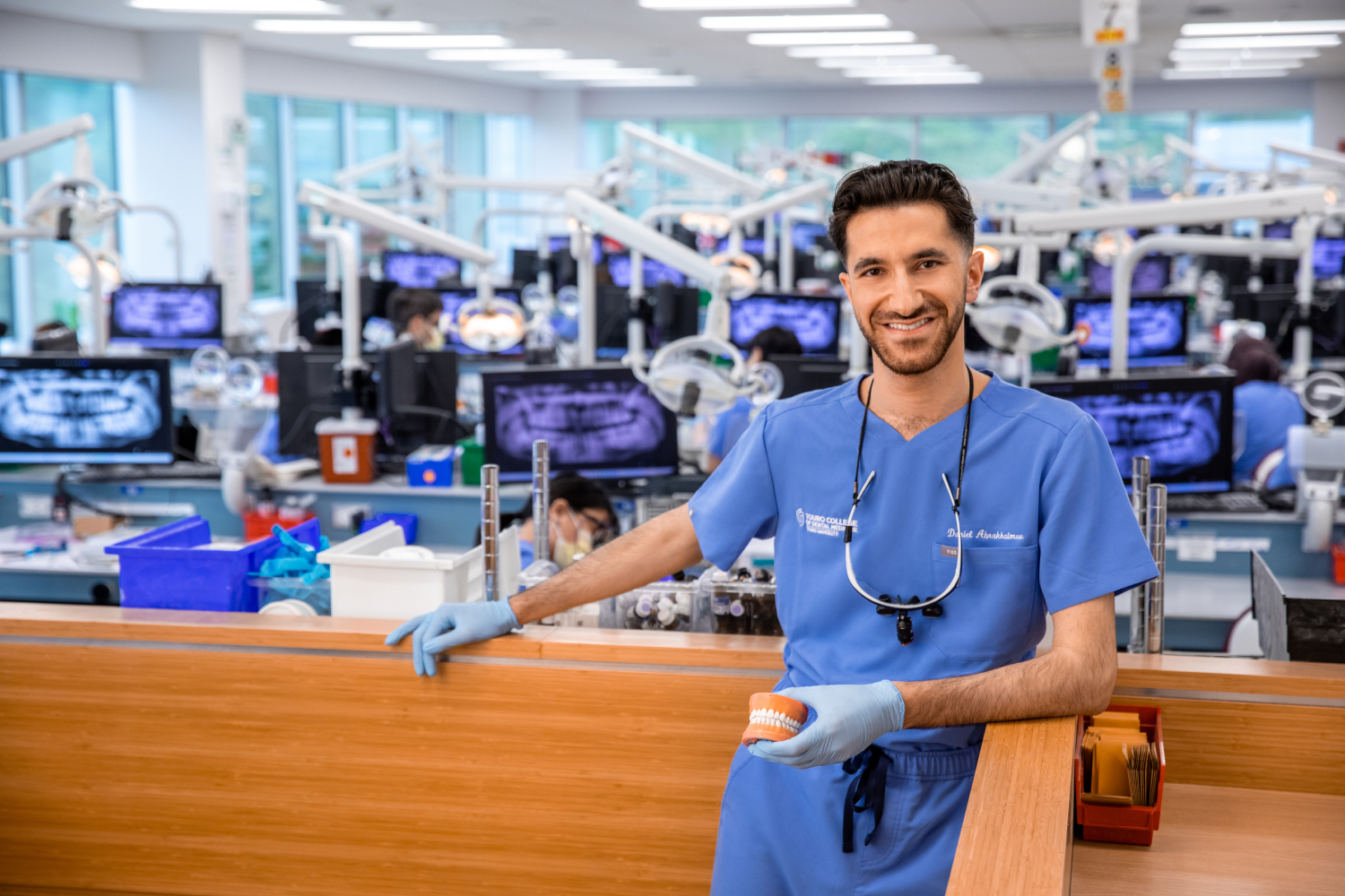 Daniel Abrakhaimov smiling in dental lab, holding a model of a mouth.