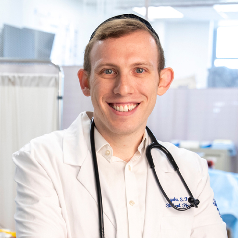 Eliyahu Freund smiling while wearing white coat and stethoscope around neck in TouroCOM practice clinic