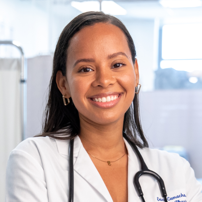 Erica Camacho smiling while wearing white coat and stethoscope around neck