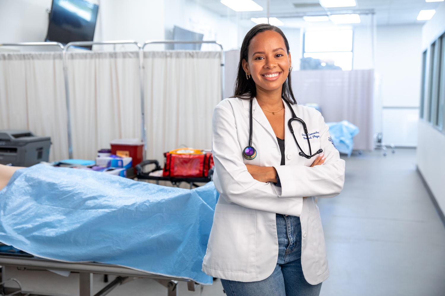 Erica Camacho smiling while wearing white coat and stethoscope around neck in practice clinic