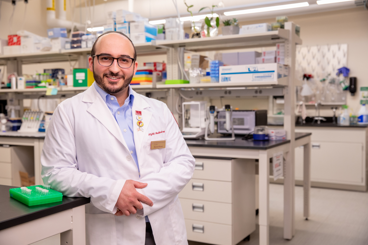 Meechael Hizami wearing white coat and smiling in NYMC lab.