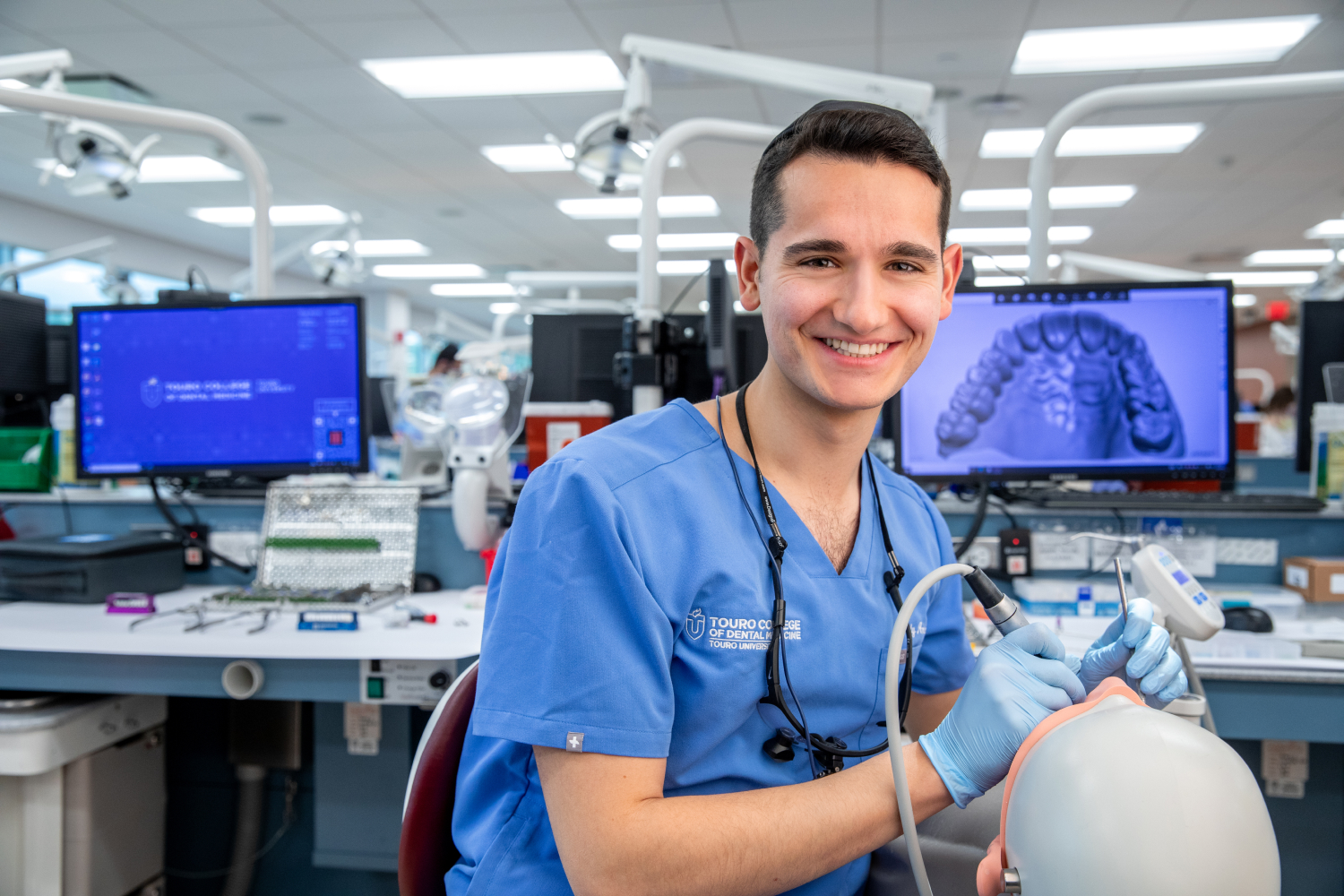 Mendy Antelis smiling in dental lab while practicing on a fake patient.