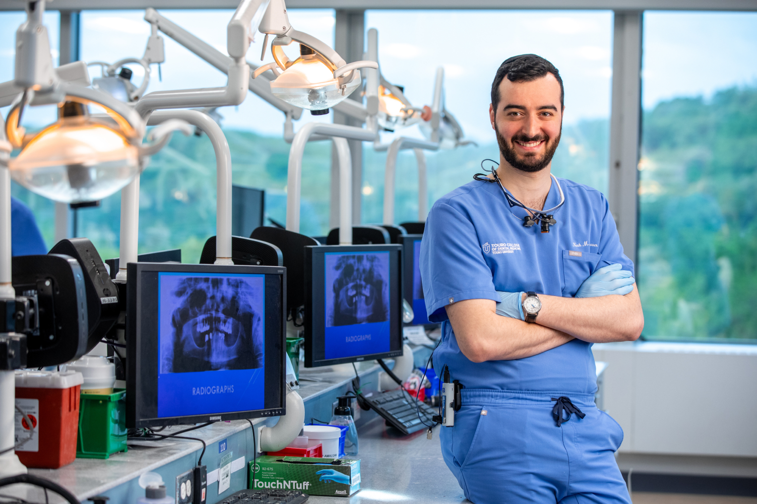 Noah Hanover smiling in front of screens with x-rays of mouths on them in dental lab.