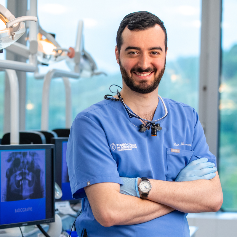 Noah Hanover smiling in front of screens with x-rays of mouths on them in dental lab