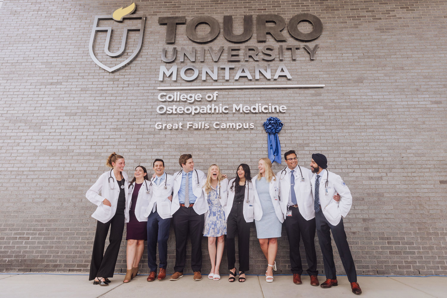 Group of TouroCOM Montana students smiling in front of sign on campus.